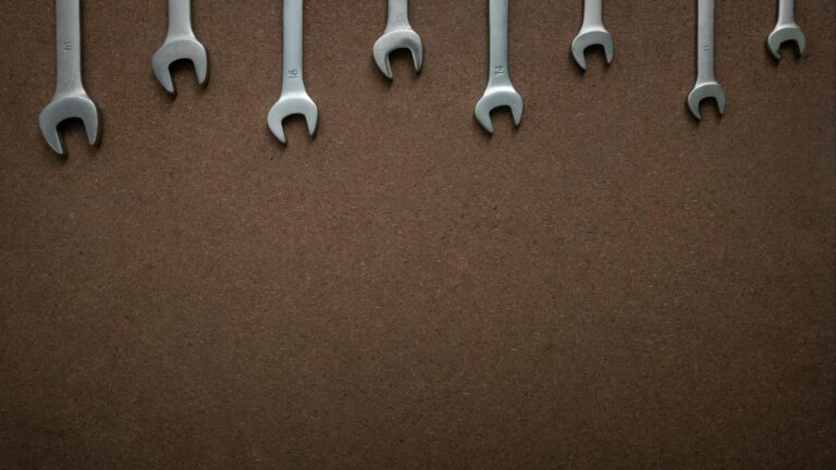 Flat lay of several wrenches lined up on a brown textured background with copy space.