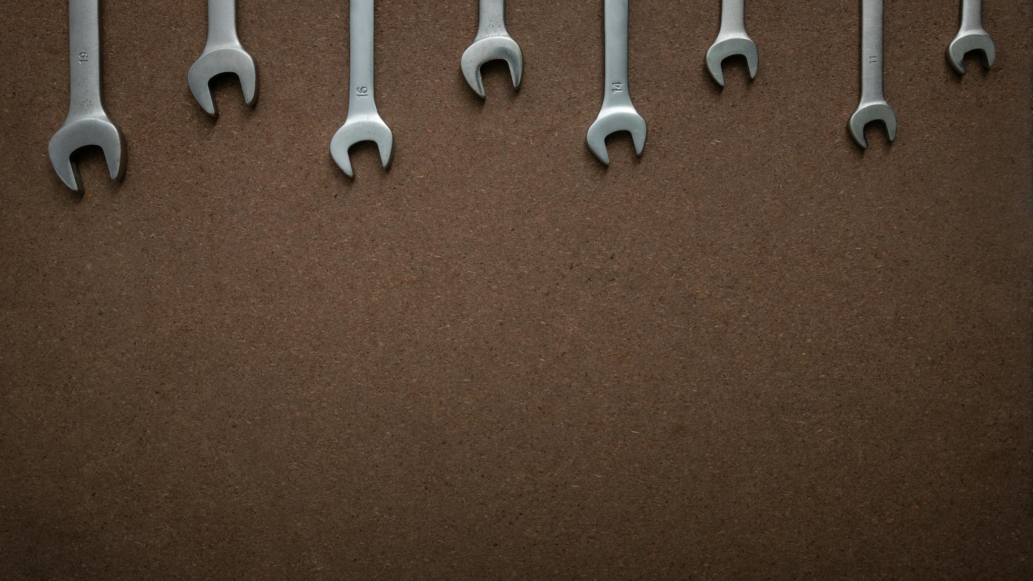 Flat lay of several wrenches lined up on a brown textured background with copy space.